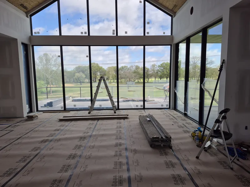 A two-story wall of windows and glass doors in a new home, with a ladder and building materials on the covered floor.