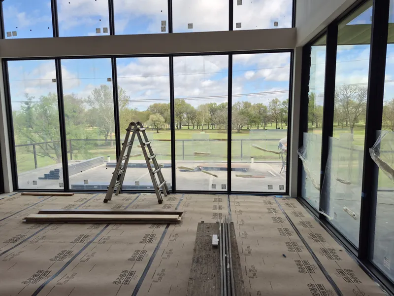 A corner of floor-to-ceiling windows in a new home, looking out over a lawn and trees.