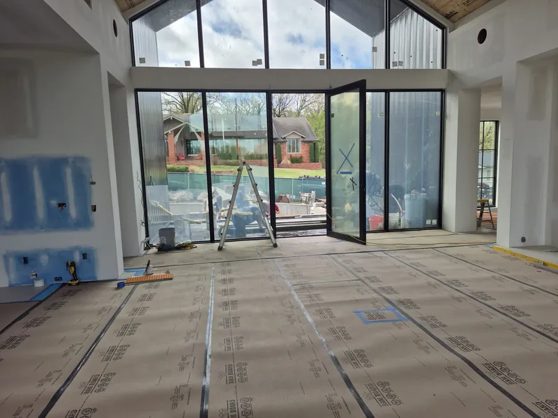A wall of glass doors under high windows in a new home, with protective paper on the floor.