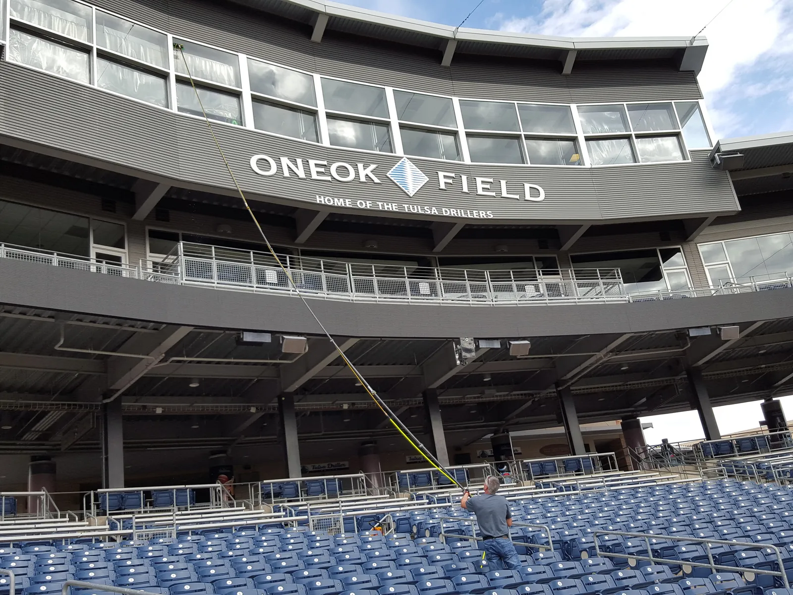A window cleaner in the stands at ONEOK Field, home of the Tulsa Drillers, reaching the upper-deck glass with a water-fed pole.