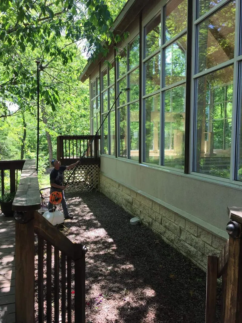 A window cleaner on a shaded path using a water-fed pole on a tall wall of chapel windows.