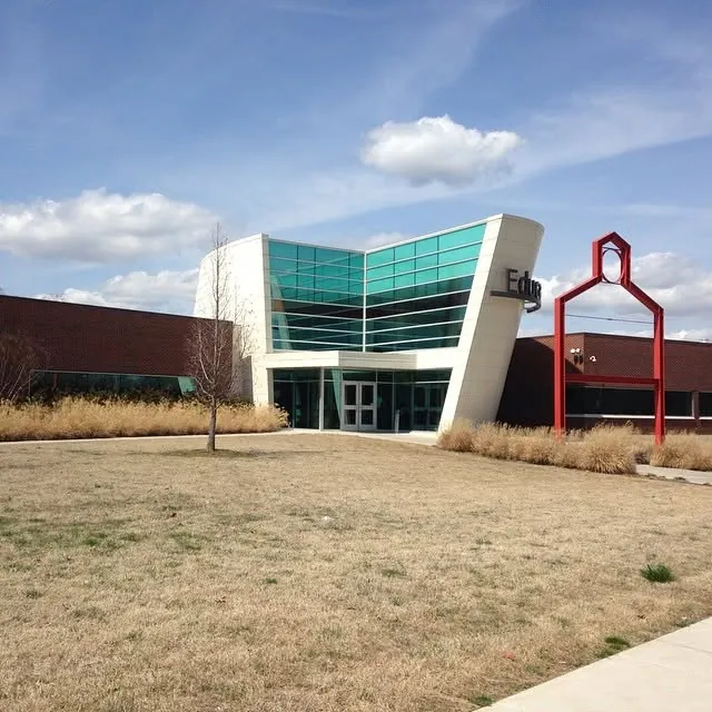 A modern building with a curved glass entrance and a red steel sculpture in front.