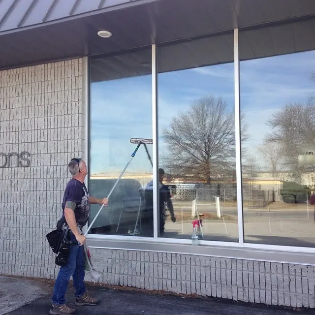 A window cleaner using a pole on the large front windows of a storefront.