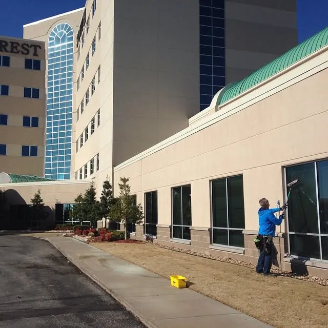 A window cleaner working on the ground-floor windows of a tall office building.