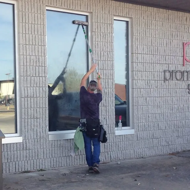 A window cleaner using a pole on a tall, narrow storefront window.