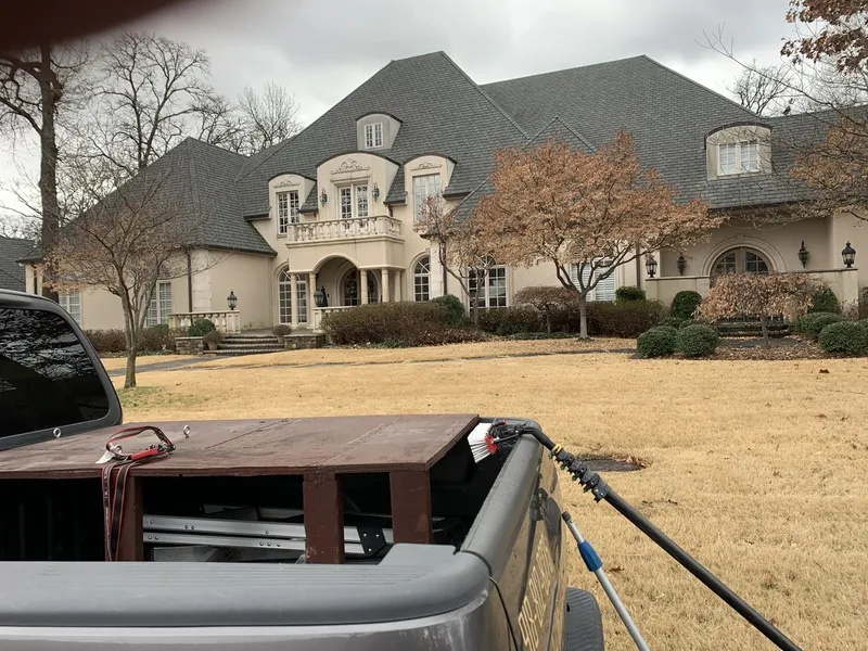 A large estate home seen across a wide lawn, with a water-fed pole in the truck bed in front.