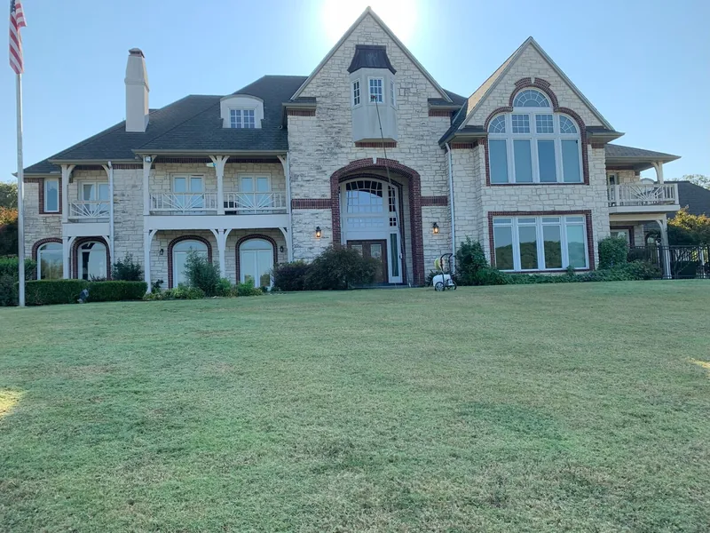 A large stone home with a tall arched entry and a green front lawn.
