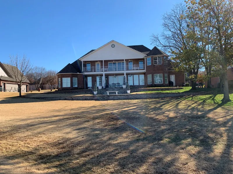 A two-story brick home with a long covered porch and a wide front lawn.