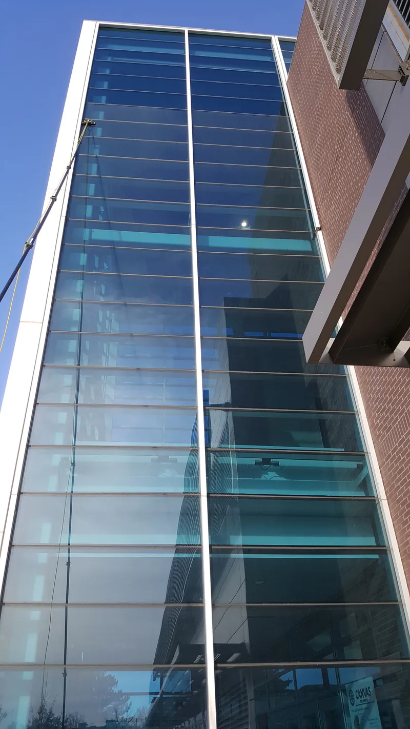 A water-fed pole cleaning a tall glass stair tower.